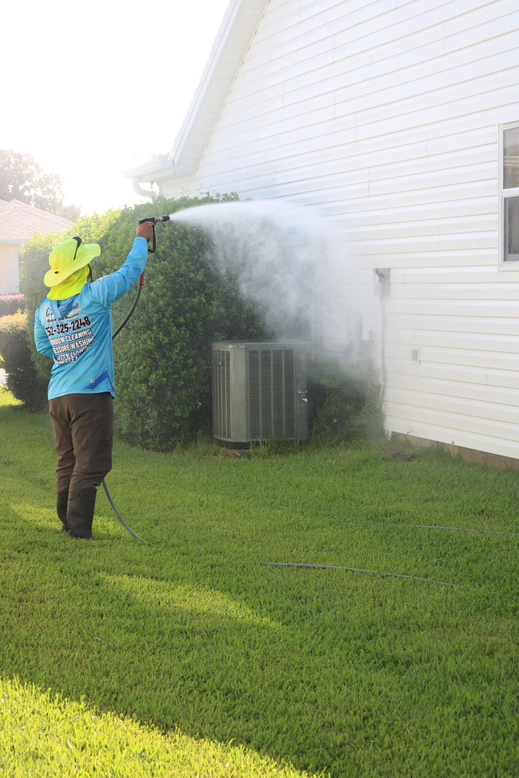 C2 Services technician soft washing siding beside a hedge and AC unit